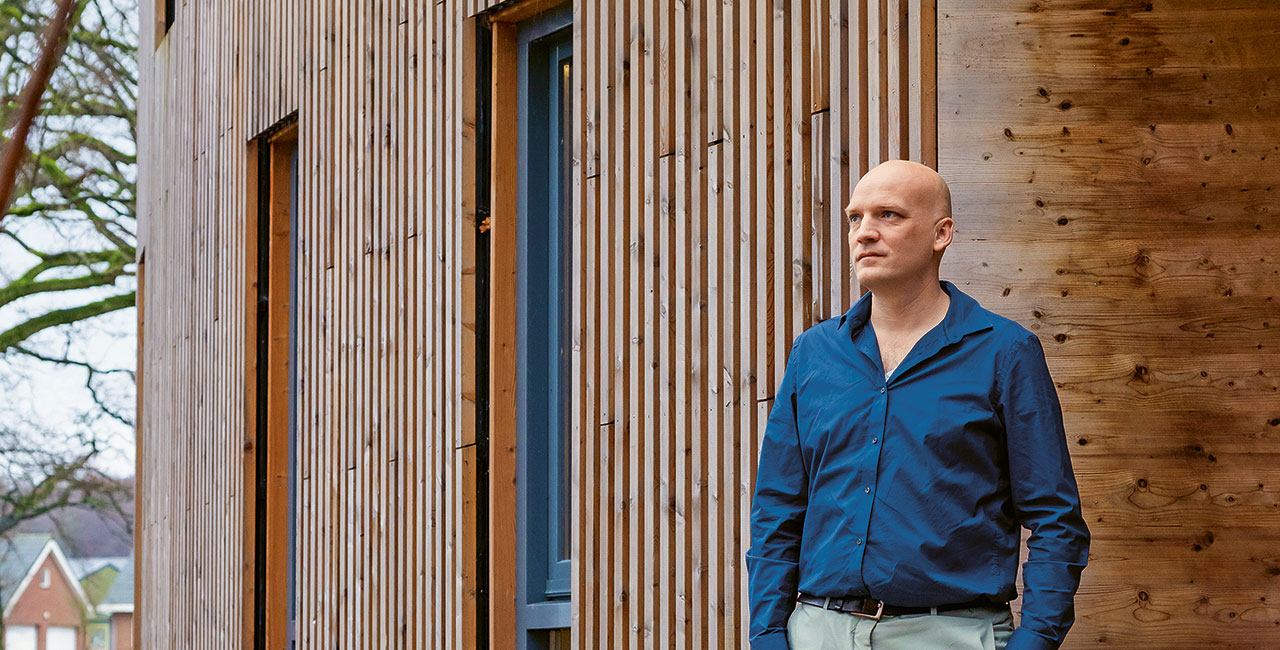 kale man met een blauw overhemd staat voor een houten huis en kijkt in de verte