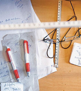 Werktafel gevuld met aantekeningen, leesbril en duimstok